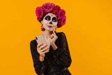 Photo of girl in halloween makeup and flower wreath using mobile phone