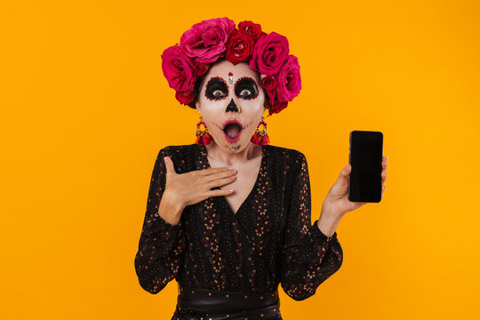 Photo of shocked girl in halloween makeup and flower wreath showing mobile phone
