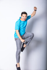 Energetic happy young Asian man in casual clothes jumping, studio shot isolated on white background