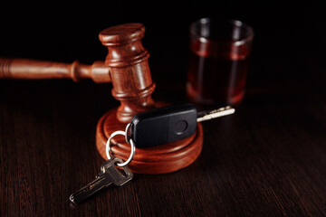 Car key, wooden judge gavel and whiskey alcohol drink in a glass on a dark table. Drink driving is...