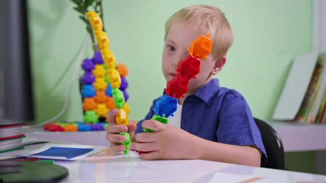 child with disabilities is playing with colorful toys while sitting at a table at home, boy with Down syndrome is studying a new constructor