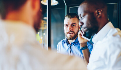 Fototapeta premium African American employer using smartphone application for discussing business project during collaboration meeting in office, diverse crew of experienced professionals developing startup in workspace
