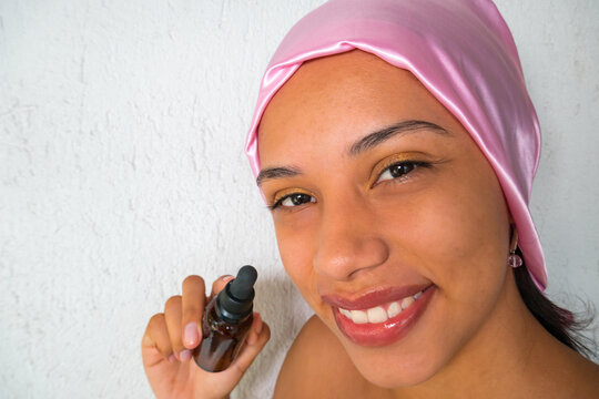 Beautiful woman with pink scarf and cosmetic oil in a bottle for moisturizing facial skin care