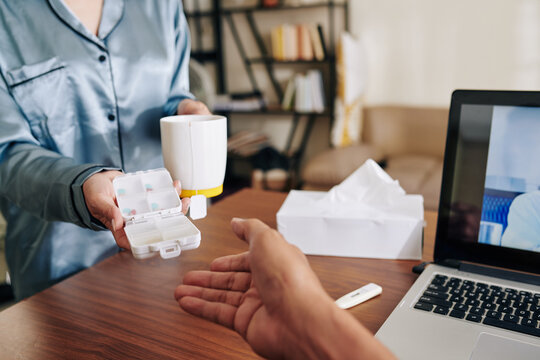 Close-up image of wife giving cup of hot tea and box of pills to sick husband