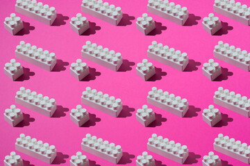 Pattern of white plastic blocks of children's constructor on a pink background