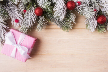 Fototapeta na wymiar Christmas background with pink gift box and frosty fir tree branches on light wooden background