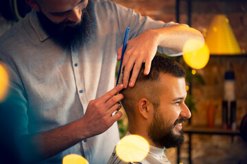 Good looking man visiting barber shop. The barber cuts his hair and trims his beard.