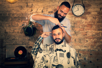 Good looking man visiting barber shop. The barber cuts his hair and trims his beard.