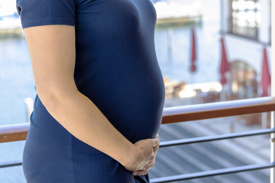Schwangere Frau in einem blauen Kleid mit Babybauch auf einem Balkon