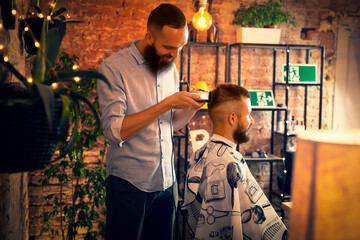 Good looking man visiting barber shop. The barber cuts his hair and trims his beard.