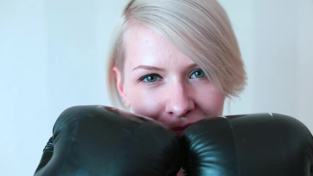 A woman in boxing gloves poses for the camera. He covers his face with gloves. Warm up before hand training. Healthy lifestyle.