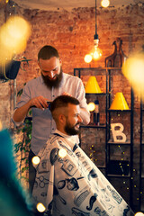 Good looking man visiting barber shop. The barber cuts his hair and trims his beard.