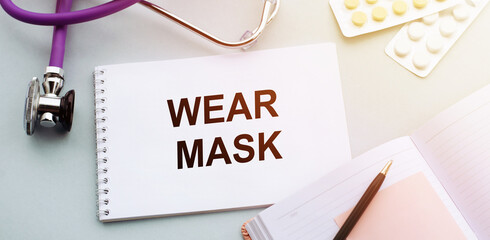 wear mask - text on notepad on medical table with stethoscope and pills