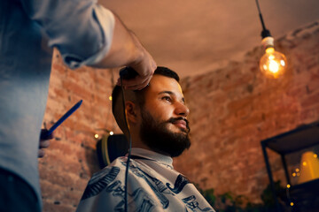 Good looking man visiting barber shop. The barber cuts his hair and trims his beard.