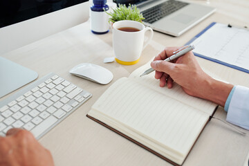 Close-up image of cardiologist taking notes in planner after examining cardiogram of patient