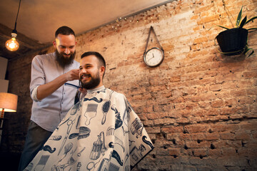 Good looking man visiting barber shop. The barber cuts his hair and trims his beard.