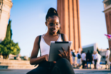Joyful young ethnic female tourist sitting on steps in city
