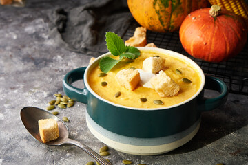 Traditional pumpkin soup puree with crackers, cream and seeds in a bowl, on a dark background