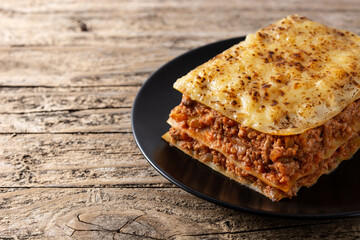 Piece of meat lasagna on black plate on rustic wooden table. Copy space	