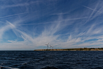 Auf See mit Blick auf Landzunge mit Windmühlen vor blauem Himmel mit Federwolken und Kondensstreifen