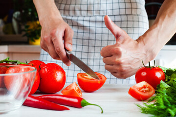 Young man cooking of vegetable salad and male hand showing thumb up. Process of making salad. Healthy food concept. Close-up.