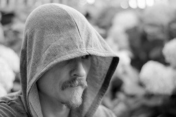 Monochrome image of a man in a hood. A man with a beard and mustache covered his head with a hood...