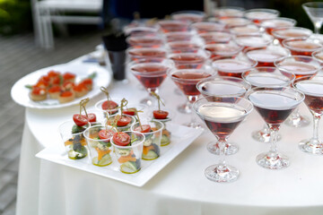 Set of cold snacks, with canapes in the foreground. In the background drinks in beautiful glasses.