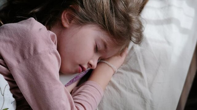 little sleeping girl lies in bed with closed eyes, close up