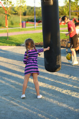 Obraz premium Back portrait of a boxing toddler girl with a punching bag on the outdoor sports ground