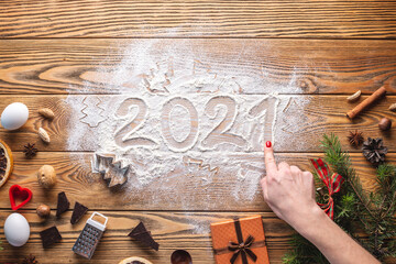 The numbers 2021 are written on flour, which is scattered on a wooden table. Concept of the New year and the cooking of holiday cookies