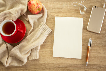 Notebook with pen, phone, sweater and cup of tea on the wooden table. Cozy autumn or winter consept. 