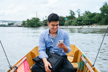 Asian business man using phone and travel by a boat in Bangkok.