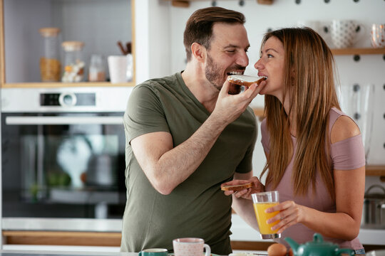 Young Couple Making Breakfast At Home. Loving Couple Eating Sandwich In Kitchen.