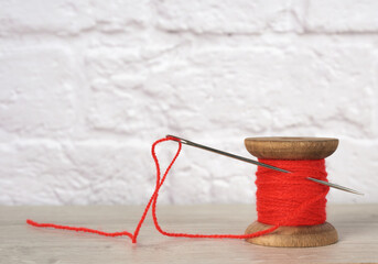 wooden spool with red wool thread on shelf, white wall