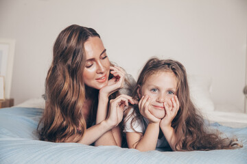 Close up portrait of happy loving family lying relaxing enjoying in bedroom together. Mother and her cute preschool daughter child girl in pajamas playing and hugging in bed. Happy mother's day.