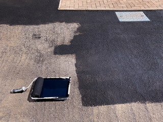 Paint roller and paint tray being used to seal a tarmac driveway with black paint