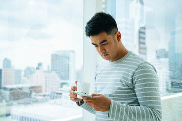 Asian man looking at smartphone and hold a cup of coffee.
