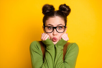 Closeup photo of attractive lady two funny buns intelligent clever student shy expression send air kisses arms cheeks wear specs green pullover brown overall isolated yellow color background