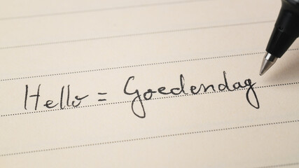 Beginner Dutch language learner writing Hello formal word Goedendag for homework on a notebook