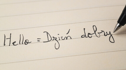 Beginner Polish language learner writing Hello formal word Dzien dobry for homework on a notebook © Keitma