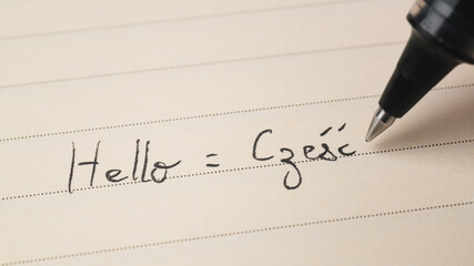 Beginner Polish language learner writing Hello word Czesc for homework on a notebook
