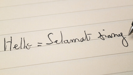 Beginner Indonesian language learner writing Hello formal word Selamat siang for homework on a...