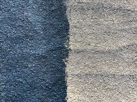 Contrast between part of a driveway painted with black sealant paint and part unpainted. No people. Copy space.