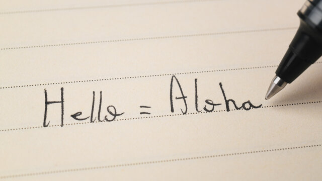 Beginner Hawaiian language learner writing Hello word Aloha for homework on a notebook