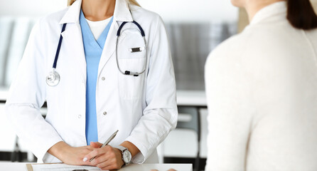 Unknown woman-doctor and patient in hospital. Blonde physician controls medication history records and exam results while using clipboard, close-up. Medicine concept