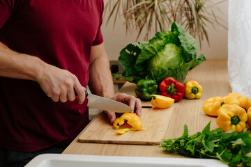 Happy handsome man is cooking in the kitchen by the window. Cut vegetables. Fresh bell peppers, cabbage and mint. Harvesting. selective focus
