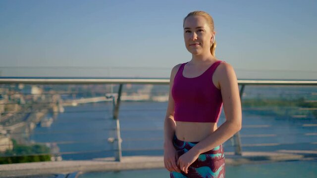 A slender young girl athlete on the background of the city. Girl with wireless headphones. 4K