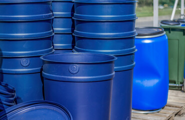 Huge blue buckets stand on wooden pallets. A blue barrel and a green tank can be seen in the background.