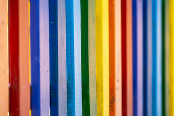 Part of wooden, rainbow colorful painted fence  on a sunny hot summer day in a city park. Abstract multicolored background.