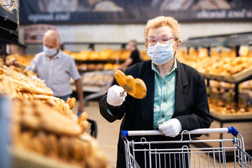 older woman with glasses chooses buns and bread in supermarket bakery
